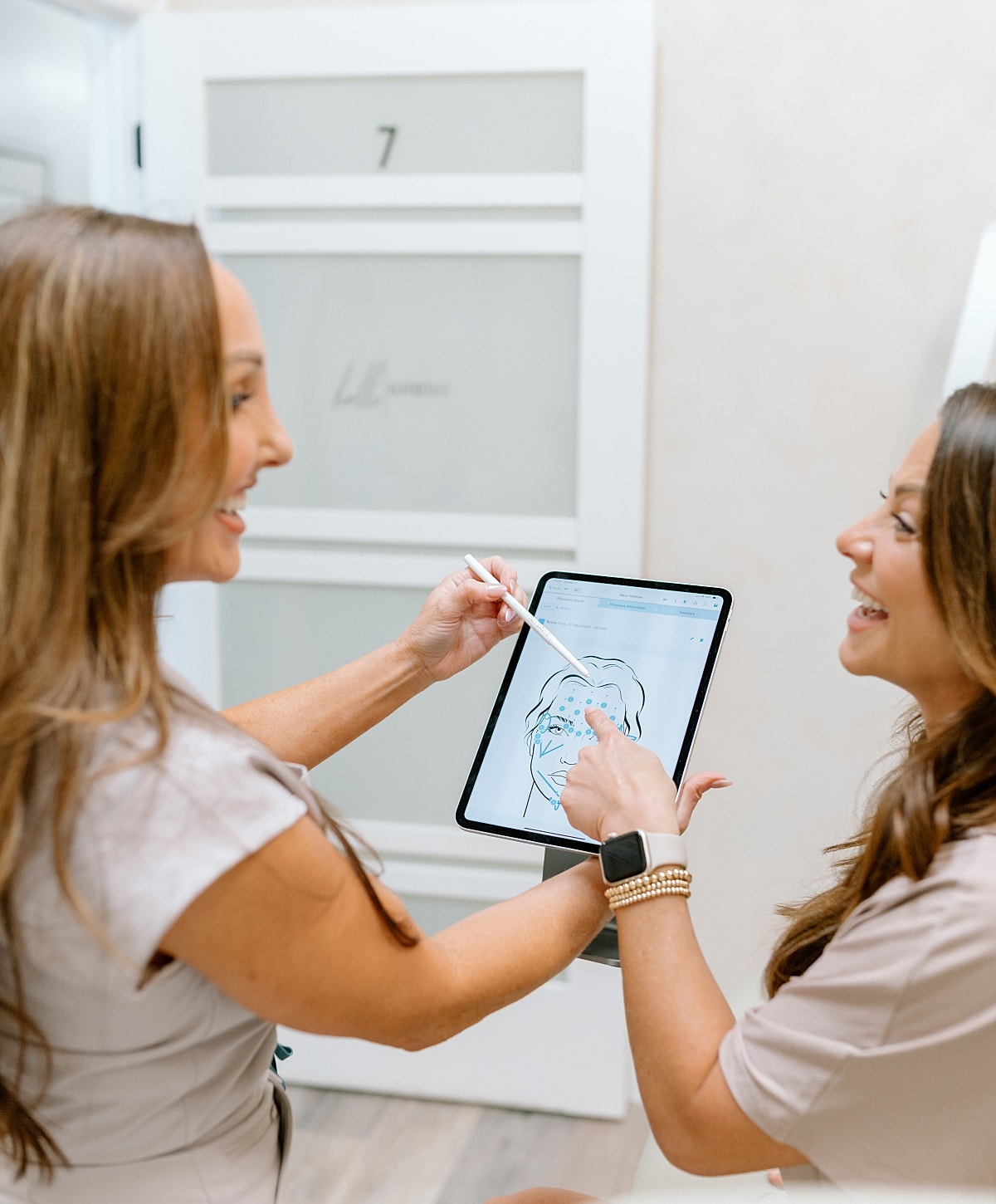 Women discussing facial treatment with digital tablet.