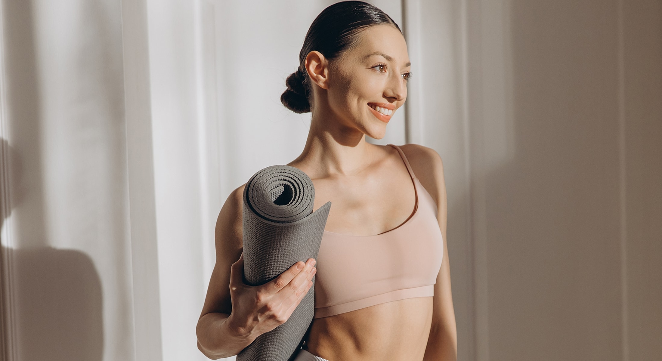 Smiling woman holding a yoga mat indoors.